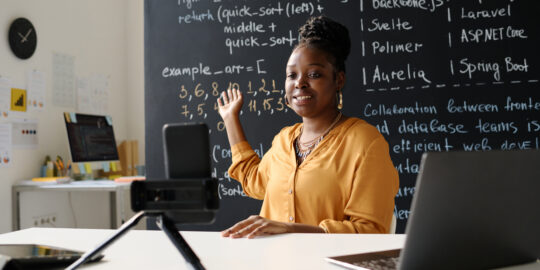 African American teacher leading her blog online about IT while sitting at table in front of smartphone on tripod