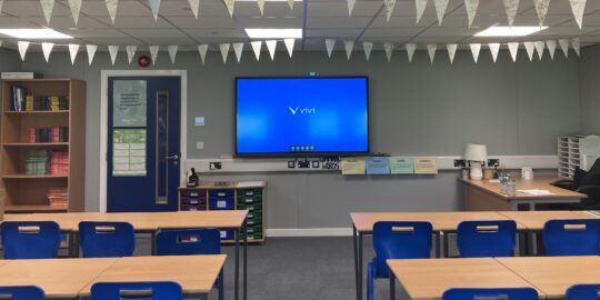 A school classroom with Vivi seen on TV display.