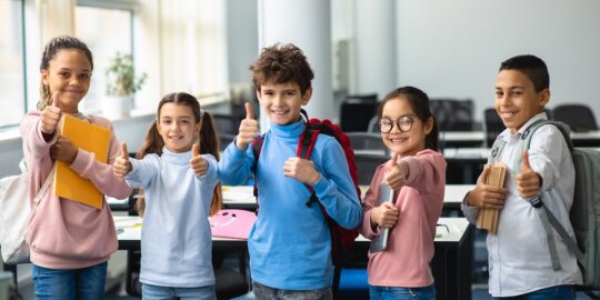 Smiling international schoolchildren showing thumbs up gesture