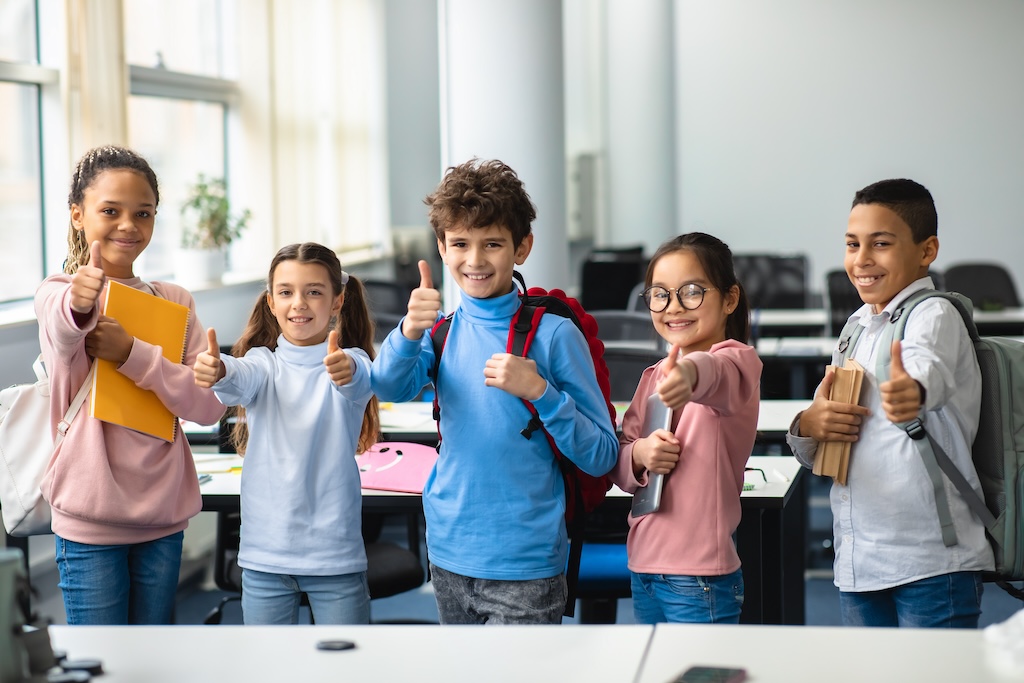 Smiling international schoolchildren showing thumbs up gesture