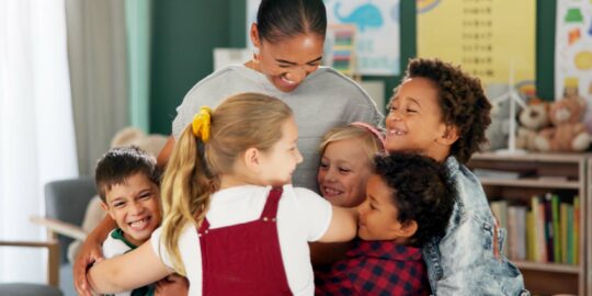 Happy woman, kids and hug teacher at school for learning, education or development in class together. Smile, group and children embrace educator in kindergarten for diversity, study or playing game.