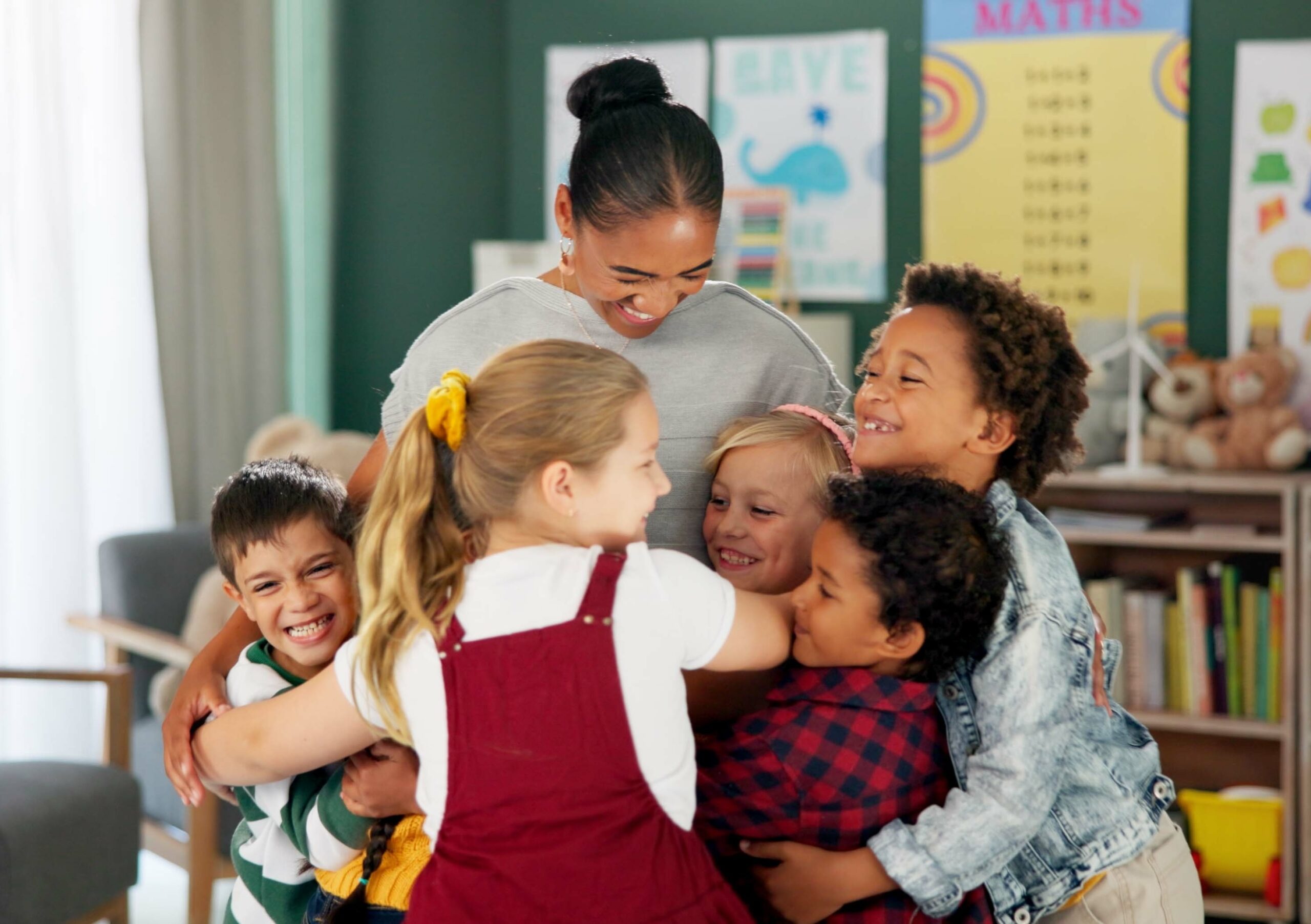 Happy woman, kids and hug teacher at school for learning, education or development in class together. Smile, group and children embrace educator in kindergarten for diversity, study or playing game.