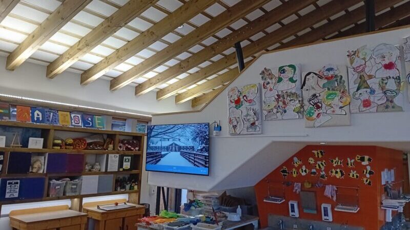 Inside view of an art classroom at Amesbury School with a digital display hanging on a wall adjacent to student artwork.